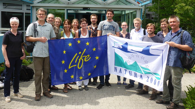 Group of people with EU-LIFE and Natura 2000 flags in front of a building
