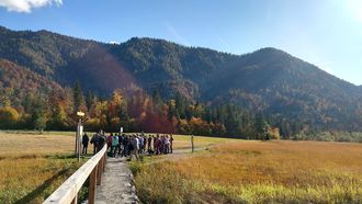 Menschengruppe steht in einer Landschaft vor Bergen