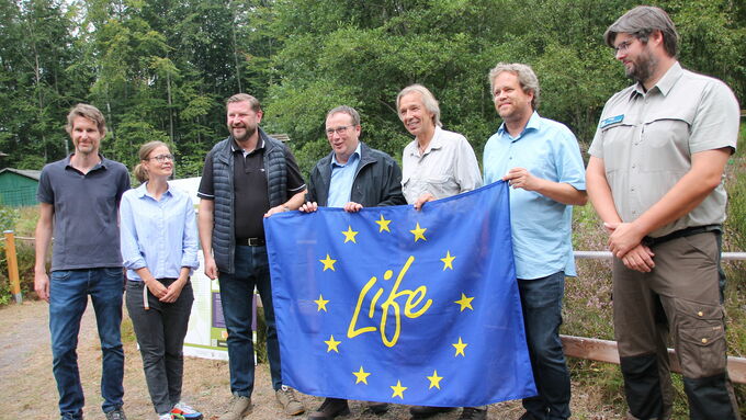 Zum obligatorischen Gruppenfoto mit der LIFE-Fahne versammelten sich zum Abschluss Georg Keggenhoff (Nationaler Kontakt EU LIFE im MUNV), Claudia Wackerl (Abteilungsleiterin Grün und Freiflächen im Stadtdienst Natur und Umwelt der Stadt Solingen), Oberbürgermeister Tim Kurzbach, Umweltminister Oliver Krischer, Dr. Jan Boomers (Geschäftsführer Biologische Station Mittlere Wupper), IP-LIFE-Projektleiter Dr. Sebastian Schmidt (Bezirksregierung Münster) und Revierförster Benjamin Klask.